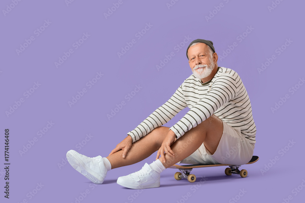 Fototapeta premium Senior man sitting on skateboard against lilac background