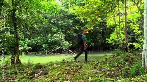  Man walking alone in the Amazon rainforest near a river, enjoying nature.