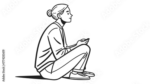 Woman sitting cross legged holding a phone looking to the right with a bun wearing casual clothes