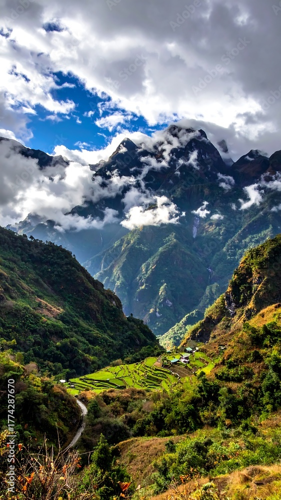 Fototapeta premium A steep valley with green terraces leads to mist-shrouded, rugged mountains