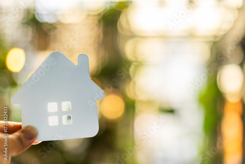 Hand holding white house symbol with soft bokeh background represents dream home, real estate ownership, residential lifestyle, eco housing, and family life concept in property investment.