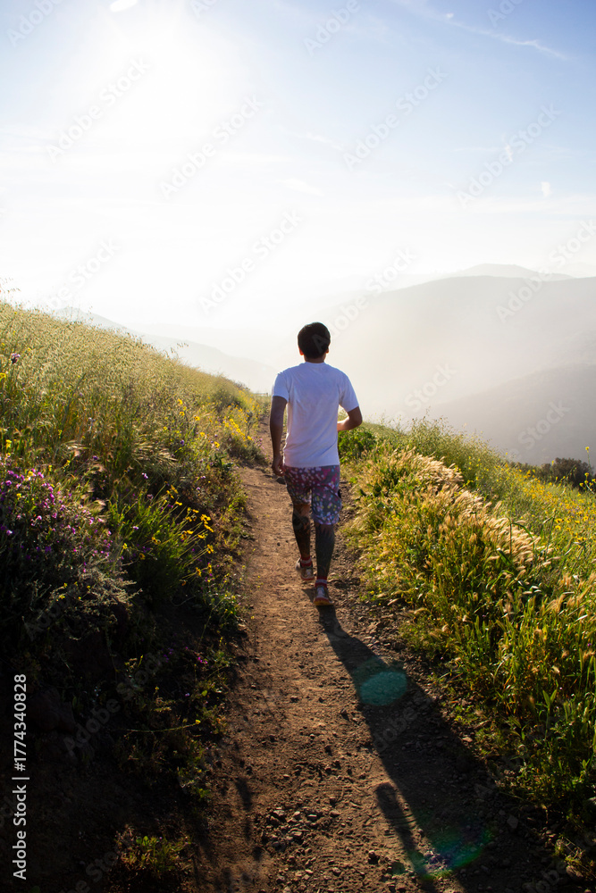 Naklejka premium Man jogging on dirt trail through spring wildflowers at sunrise