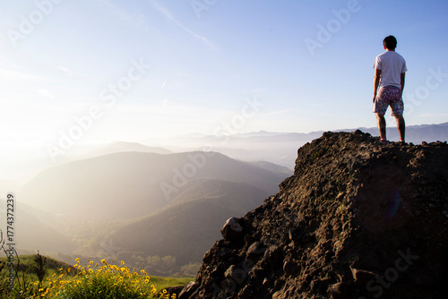 Man standing on rocky cliff overlooking misty mountain valley, sunrise