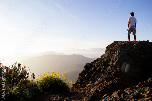 Man on rocky summit gazing at sunlit misty mountain landscape