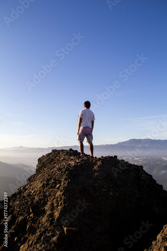 Man standing on rocky peak overlooking hazy mountains at sunrise