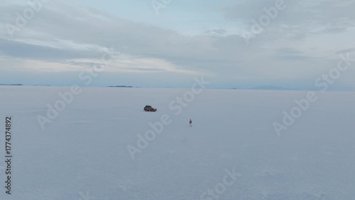 Aerial drone shot of a 4x4 driving across the endless white expanse of the Salar de Uyuni on a bright summer morning surrounded by reflections and the silence of the Bolivian altiplano