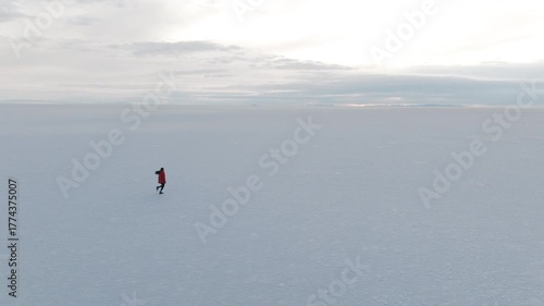 Aerial shot of a woman walking slowly across the vast and endless Uyuni salt flats in Bolivia surrounded by silence and natural beauty