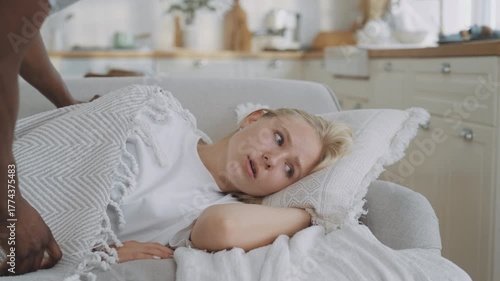 Unhappy blonde woman lying on couch, african man stroking head, careful husband. Depression and frustration, bad mood in autumn day, melancholy or seasonal viral disease, autumn blues and sadness
