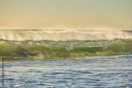 Waves build in power as they race to the shore, backlit by the rising dawn light