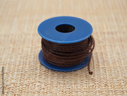 Brown cord on a blue spool sitting on a woven surface in a studio setting image shot