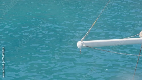 High-angle shot looking down at the stunningly clear, turquoise water from the bow of a sailboat or yacht.