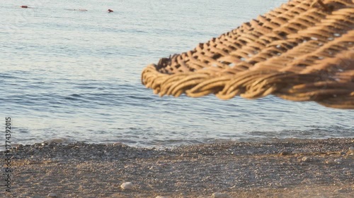 Relaxing holiday scene with a woven straw beach umbrella visible in the foreground and gentle sea waves washing over a pebble beach.