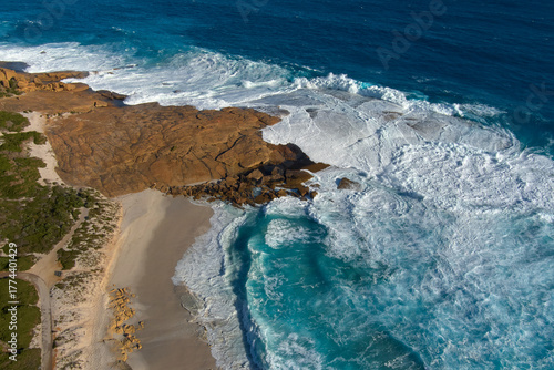 waves wrap around the rocky outcrop as the blue waters paint the rock in white foam