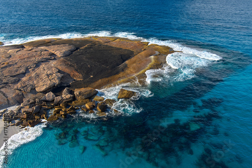 Waves cover a large rock as the crystal clear blue waters reveal the reef below its surface