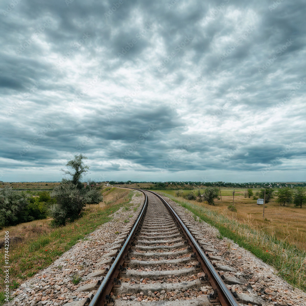 Obraz premium Train tracks stretching into a cloudy vast landscape