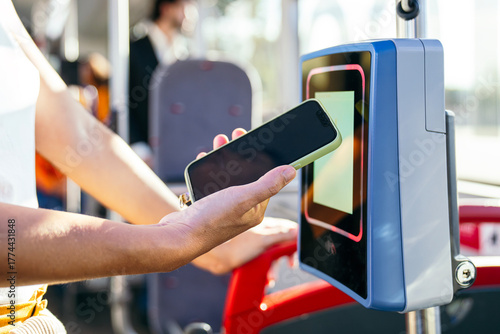 Fotografia Woman using mobile payment on a contactless reader inside a public city bus, rep