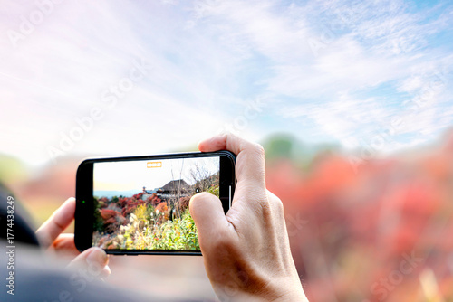 Closeup and back view hand of tourist hold and taking photography by smartphone on Kiyomizu-dera temple in Kyoto, Japan with natural red maple leaves and blue sky background.