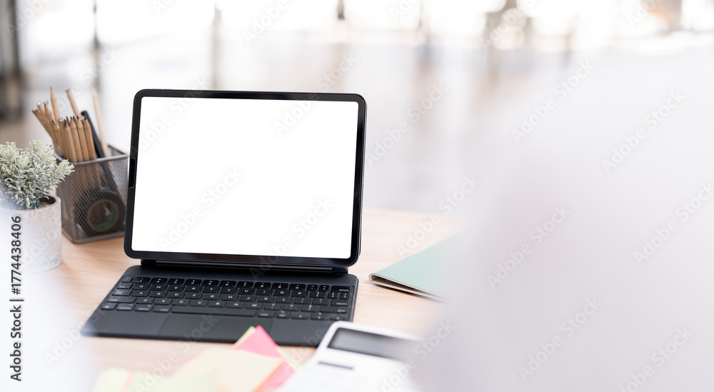 Fototapeta premium Close-up shot of a modern tablet with a blank white screen attached to a keyboard case, resting on a wooden desk in a bright office environment.