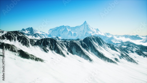 Lush snow blankets towering mountain peaks under a bright blue sky. The sunlight highlights the textures and contours, creating a breathtaking winter landscape.