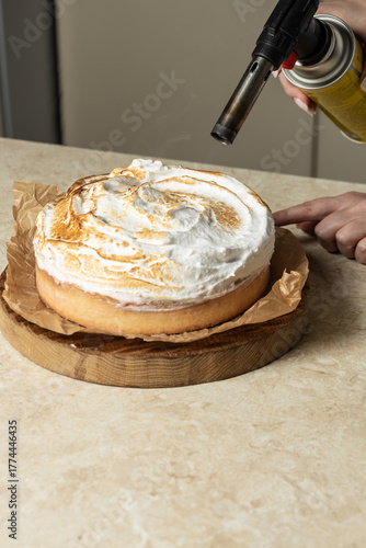 Fotografie A chef uses a culinary torch to caramelize the meringue on a round cake