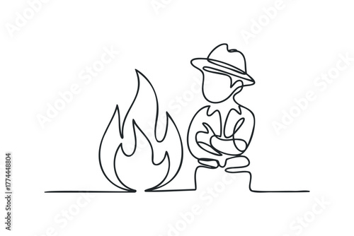 Man in hat stands by campfire with arms crossed