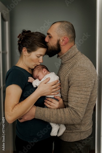 A couple stands close together in a hospital room, gazing at each other with joy. A newborn baby is in a crib nearby, creating a warm and intimate atmosphere.