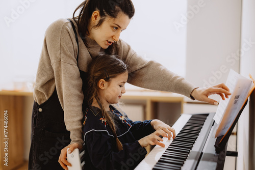 A young girl learning to play the piano with guidance from a teacher.