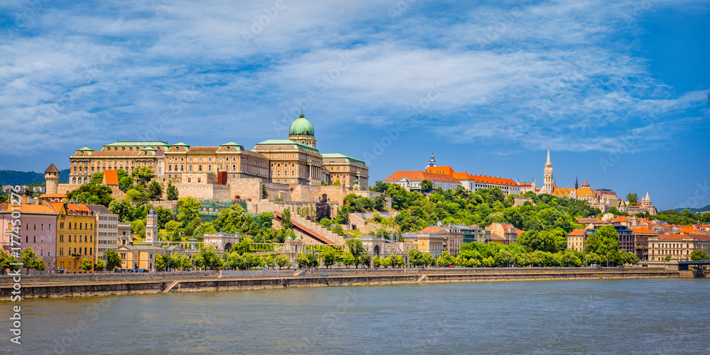 Obraz premium Panoramic view of Buda Castle and Castle Hill in Budapest, Hungary, with Matthias Church above the Danube—historic terraces and a riverside skyline under a clear summer sky.