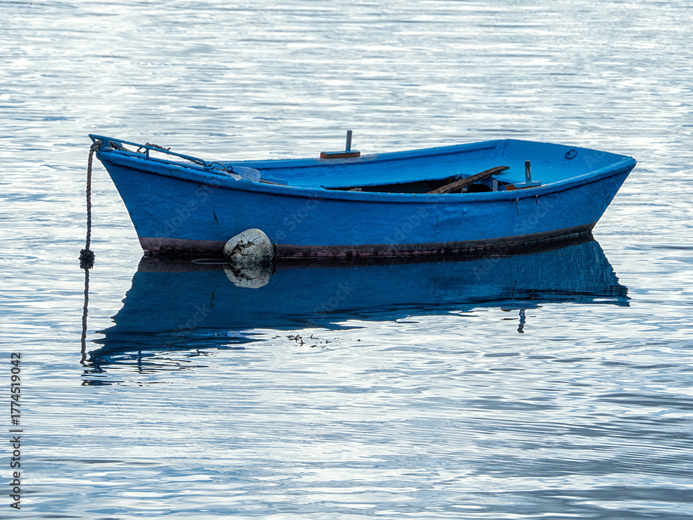 Naklejka premium Barca de pesca de color azul intenso amarrada en medio del mar en calma