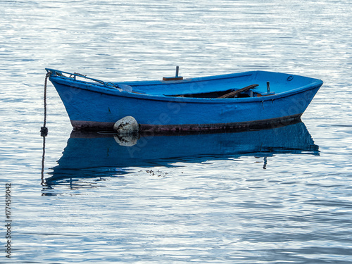 Barca de pesca de color azul intenso amarrada en medio del mar en calma