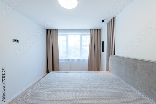 Wide Angle of Home Bedroom Interiom. King Size Double Bed and Windows in Background. White Walls.