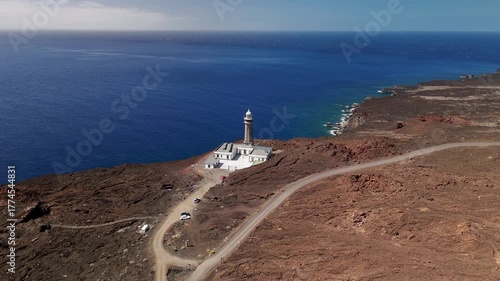 Aerial drone approach flying toward the isolated Faro de Orchilla Lighthouse situated on the rugged volcanic cliffs of Punta Orchilla, El Hierro, Canary Islands, Spain.