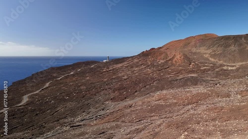 Rising aerial drone flight over the dramatic volcanic landscape of El Pinar approaching the iconic Faro de Orchilla Lighthouse on the rugged coast of El Hierro, Spain.