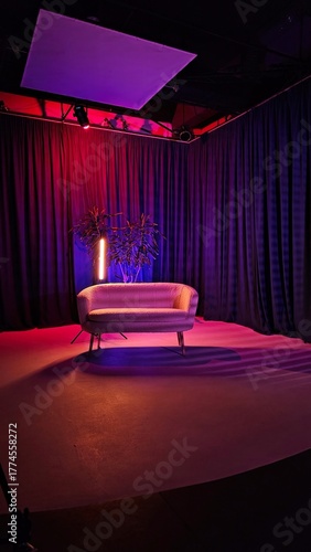 Modern couch sits against dark curtains, illuminated by vibrant colored lights. The atmosphere is artistic and inviting, perfect for a photoshoot or video production.