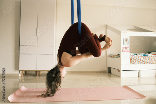 Woman practicing inverted aerial yoga pose at home
