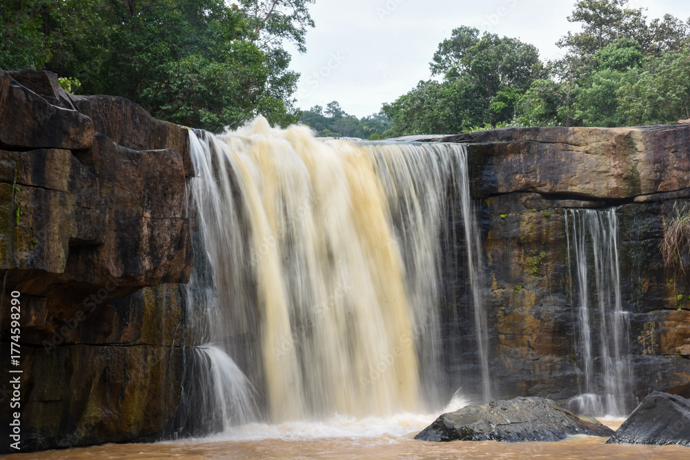 Fototapeta premium A wide waterfall of turbid water over a rocky ledge.