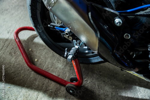 Tableau sur toile Close-up of motorcycle rear wheel and exhaust system on red paddock stand showin