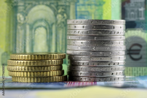 Two stacks of coins are arranged against a background of euro banknotes
