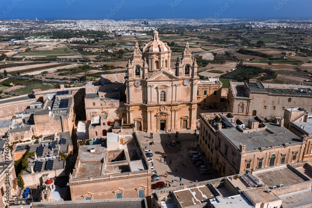 Obraz premium Aerial view of Mdina, Malta shows St. Pauls Cathedral, palazzi, and bastion walls amid fields to the Mediterranean in bright midday light with crisp warm stone