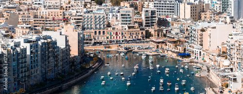 Canvas-taulu Aerial view of Sliema, Malta, with mid rise limestone and modern apartments by a sheltered inlet of boats and yachts, bright midday light, clear turquoise water, and promenades