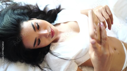 Beautiful Asian Woman Lying in Bed and Texting on Smartphone