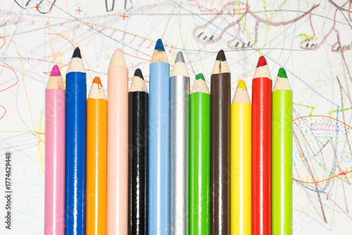 Multicolored pencils for drawing on white paper with children's drawings.