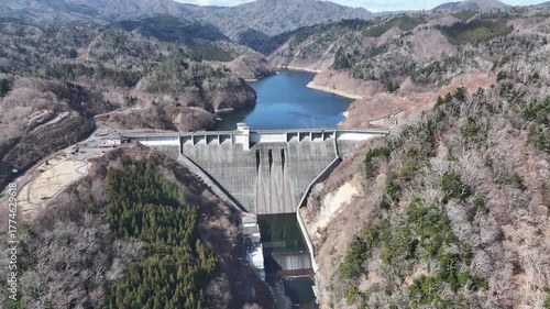 Drone footage flying over Kido Dam, revealing calm lake waters and mountain ranges beyond. Perfect for nature, travel, or dam infrastructure visuals in cinematic quality.