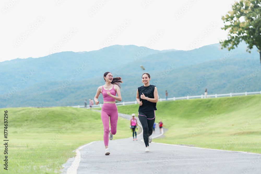 Naklejka premium Two women running on outdoor paved path in green park with mountain view and joyful expression