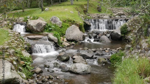 Looped footage of clear mountain stream flowing through rocks with small waterfalls and green landscape, perfect for relaxation and background scenes