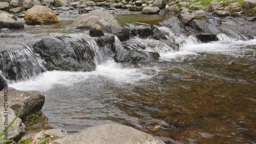 A continuous loop of clear mountain stream water flowing over brown and gray stones under natural light, perfect for relaxing and background use