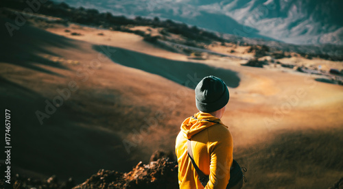 A young man walks in a desert among beautiful mountains and volcanoes at sunset.