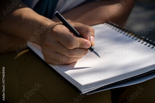 A male hand holds a pen and writes in a sketchbook, notepad closeup.