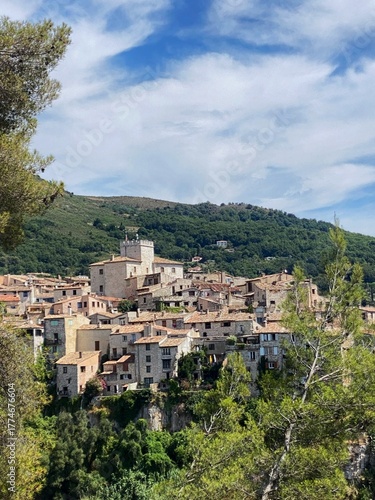 Scenic view of the medieval village of Tourrettes-sur-Loup on the French Riviera, nestled among green hills on a sunny summer day. Stone houses, lush landscape and bright Mediterranean atmosphere.