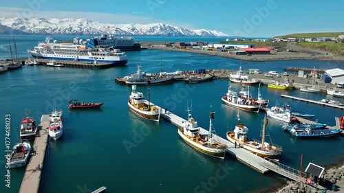 Aerial view of Husavik port filled with fishing and whale-watching boats. Calm waters reflect the bright Icelandic summer sky.